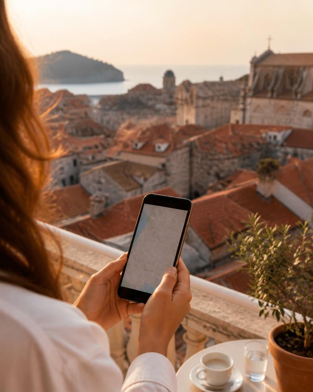A traveller checking a map on a phone from a hotel balcony above a Mediterranean old town