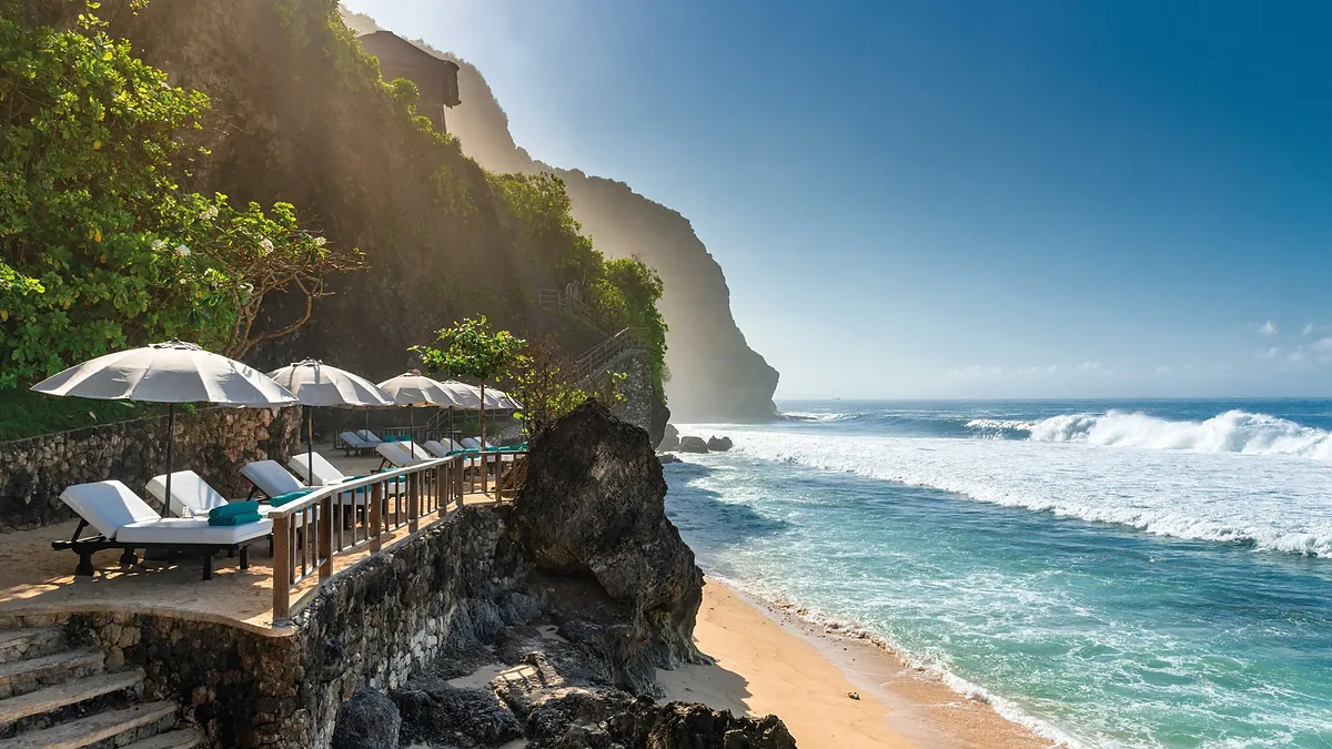 Private beach below the cliff at Bvlgari Resort Bali with loungers, umbrellas and surf