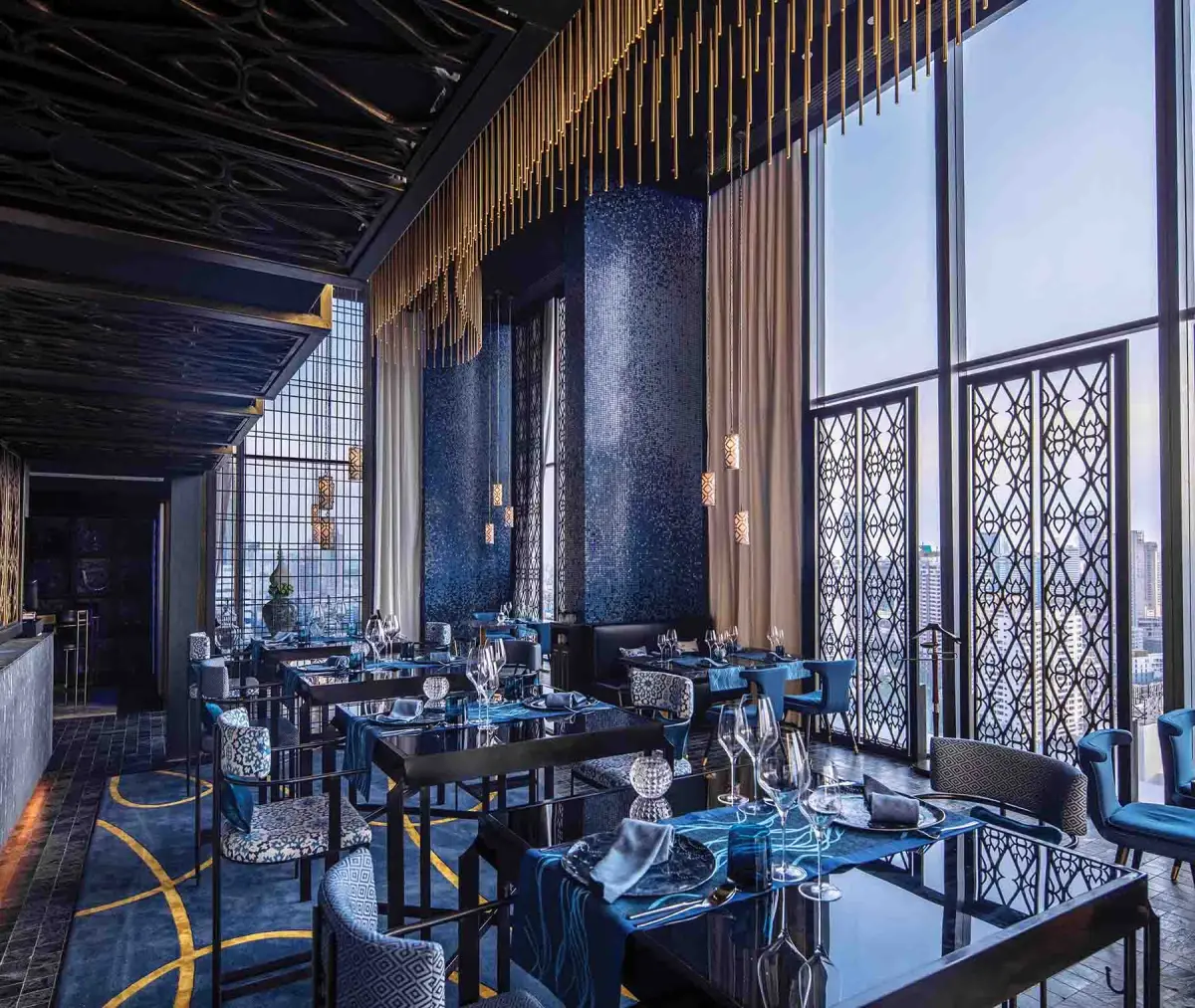 A dining room in deep blue with patterned screens and windows onto the city