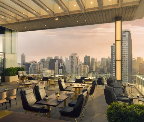 An open terrace with low chairs and planters looking over the Bangkok skyline at sunset