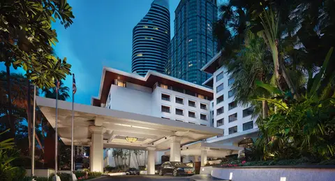 A low white hotel building among tall palms with an office tower rising behind it at dusk