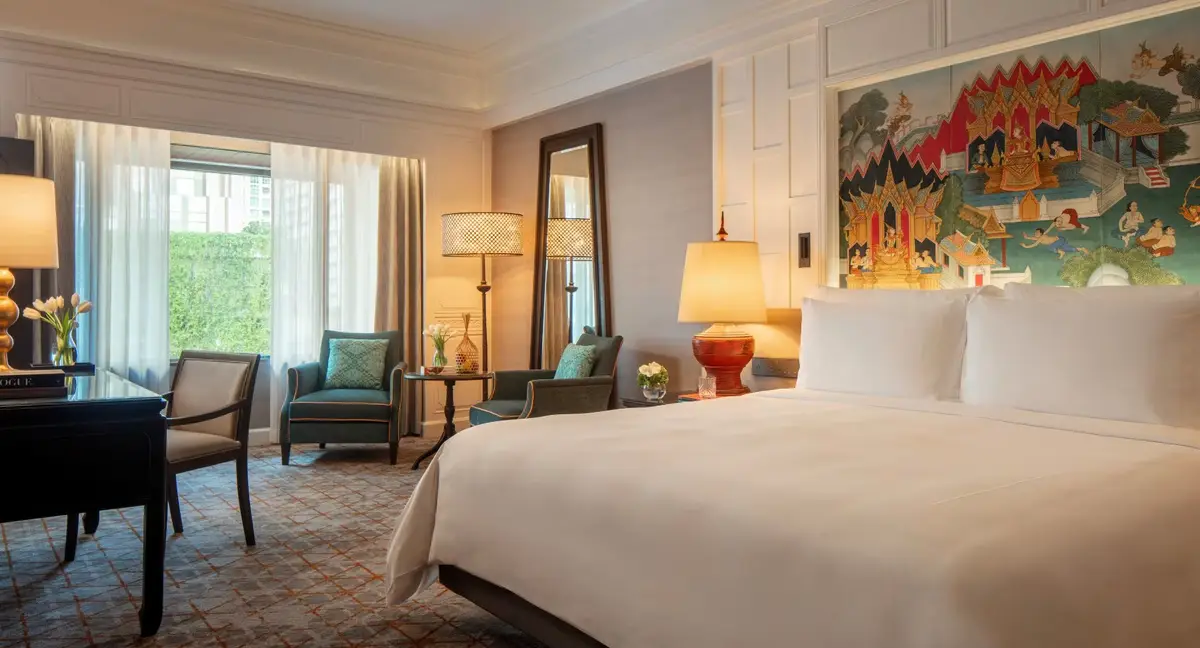 A bedroom with a Thai mural above the bed, a green armchair and a window onto trees