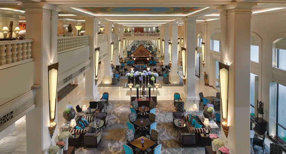 A tall lobby with white columns, hand painted murals and low seating under a gallery