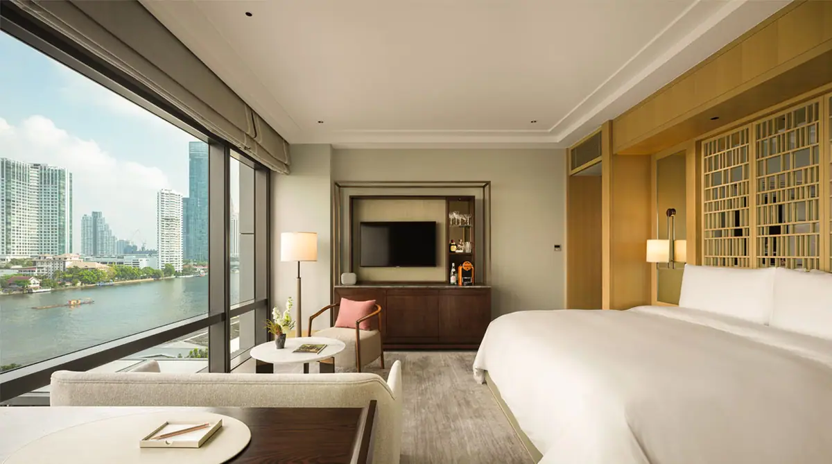 A bedroom in pale wood and stone with a wall of glass onto the river