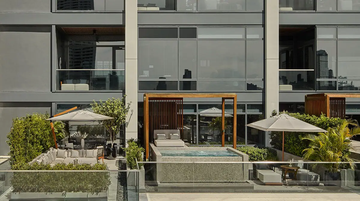 A row of plunge pools and parasols on a terrace in front of a glass hotel facade