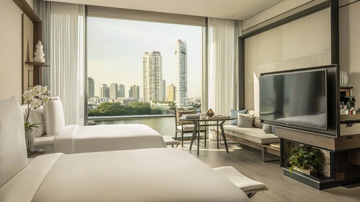 A bedroom with a pale headboard, low sofa and the river through floor to ceiling glass