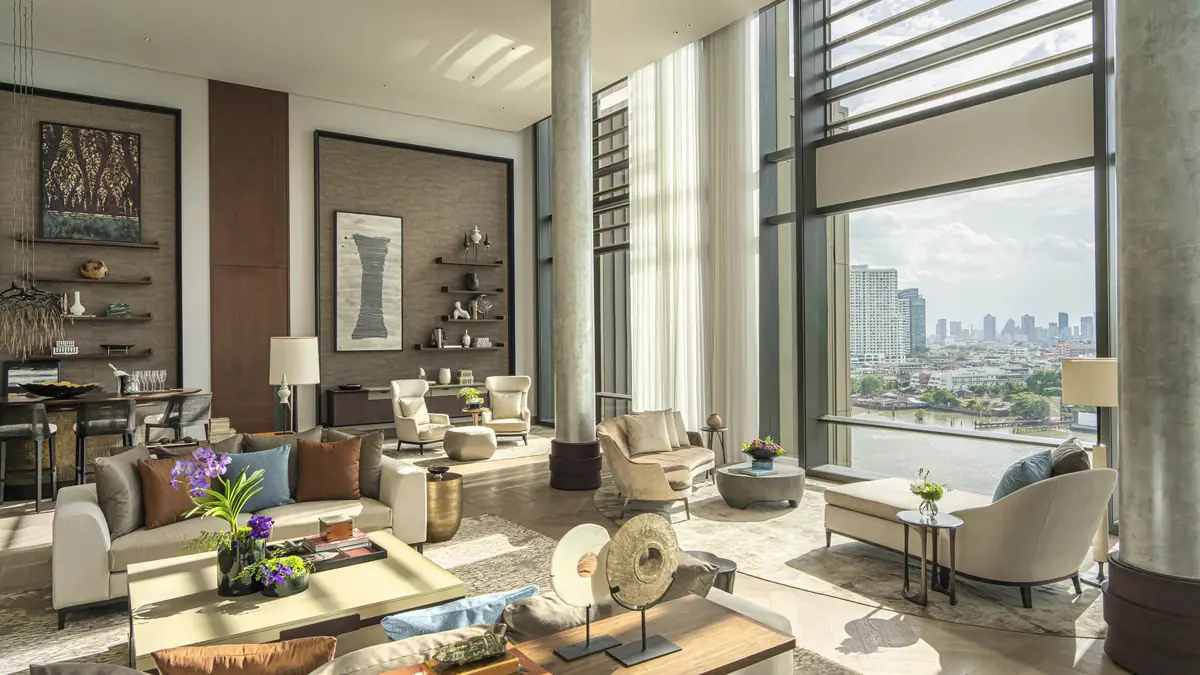A double height lounge with armchairs, art and tall windows onto the river