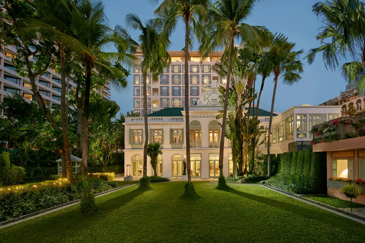 The colonial Authors' Wing of the Mandarin Oriental Bangkok lit at dusk behind tall palms