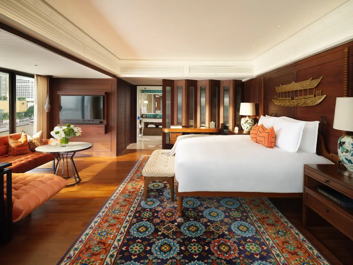 A suite bedroom with teak panelling, a patterned rug and a carved gold boat above the bed