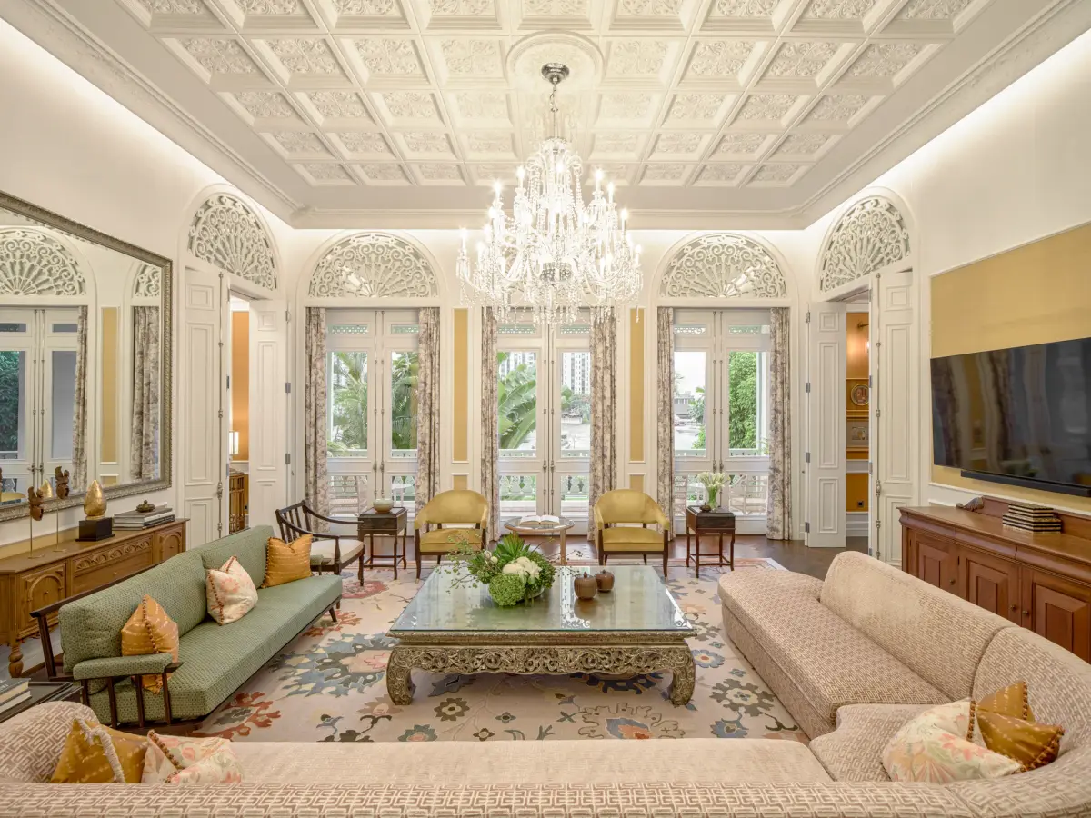 A pale green drawing room with a chandelier, moulded ceiling and tall shuttered windows