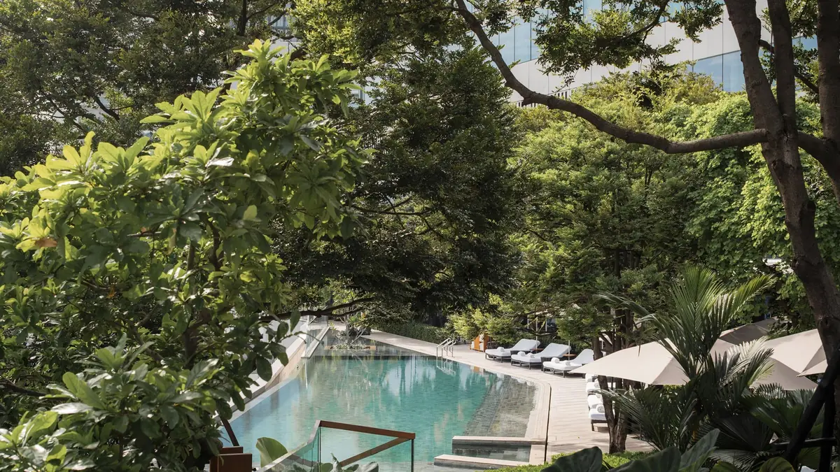 The Park Hyatt Bangkok swimming pool seen through mature trees from a shaded cabana