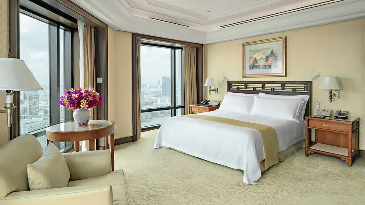 A bedroom with a dark wood headboard, orchids on a side table and the city through a wall of glass