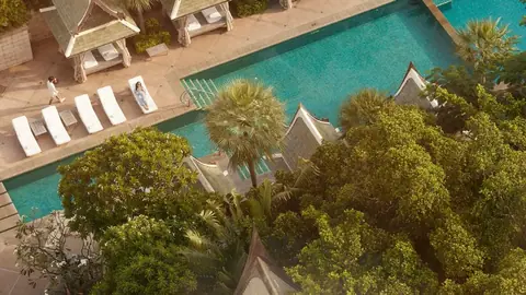 An aerial view of a three level swimming pool set among palms and Thai roofed pavilions