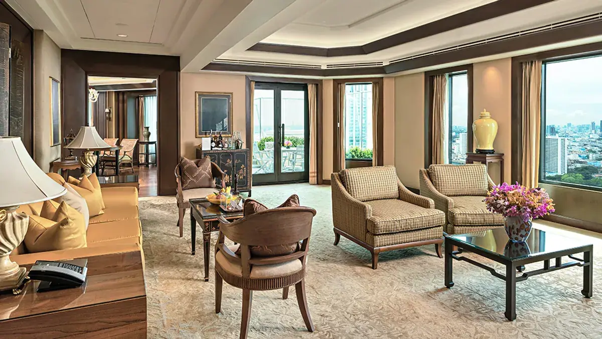 A suite sitting room in cream and teak with armchairs and sliding doors onto a balcony