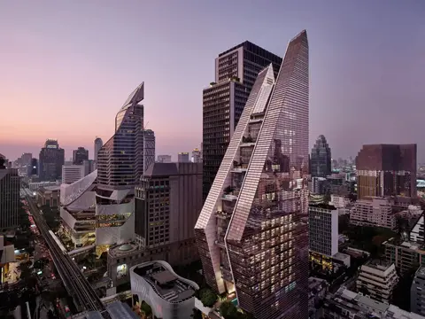 Two angled glass towers leaning towards each other above the Bangkok skyline at dusk