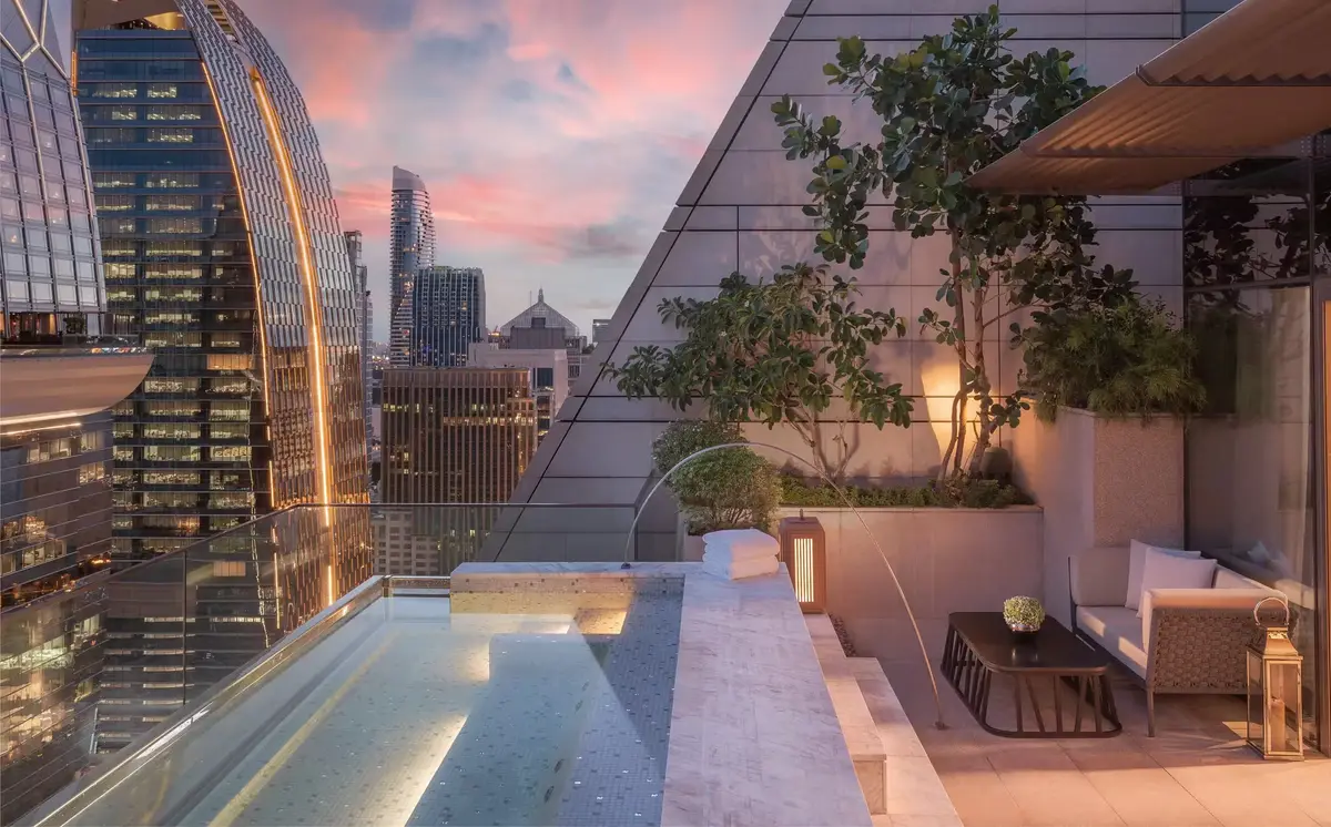 A lit plunge pool on a planted roof terrace with the city towers rising behind at dusk