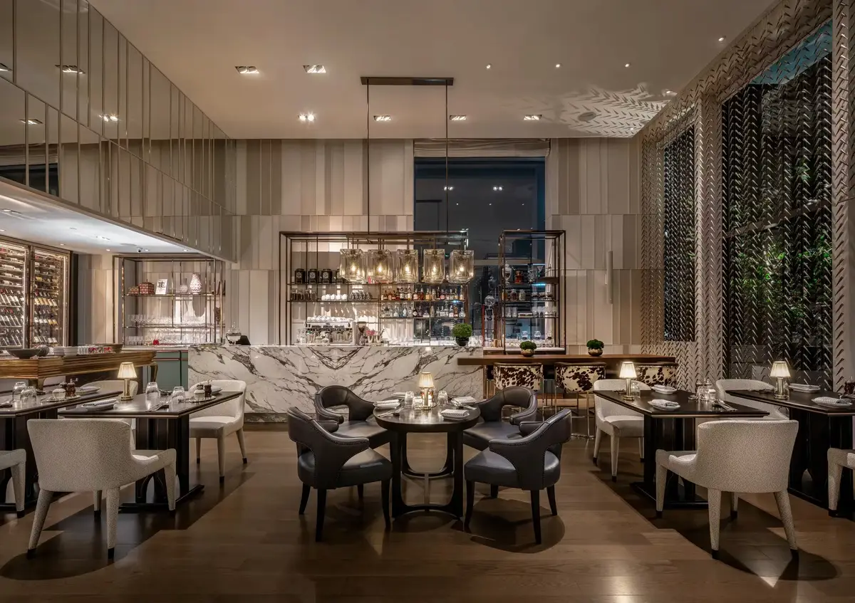 A dining room with round tables, patterned chairs and a bright chandelier over the centre