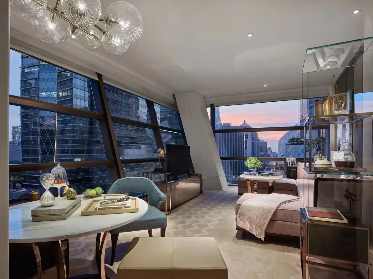 A suite living room with a long sofa, brass detailing and a chandelier under the sloping window