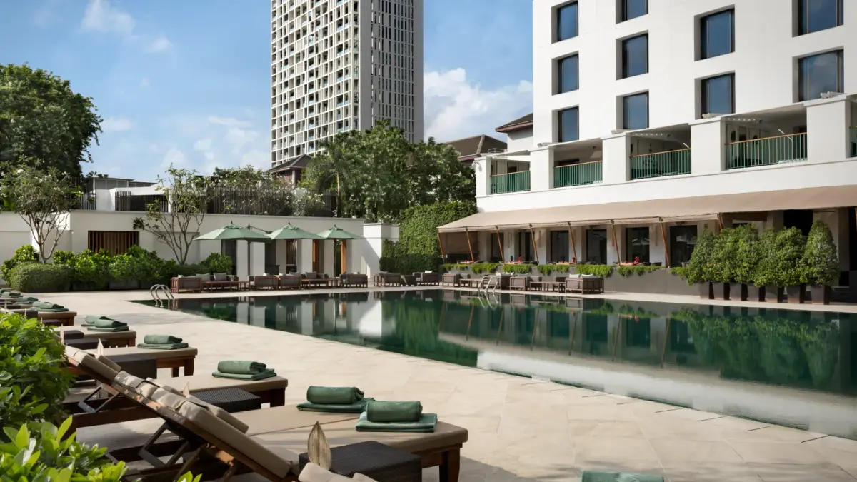 A long green tiled pool with loungers under umbrellas between two low hotel wings