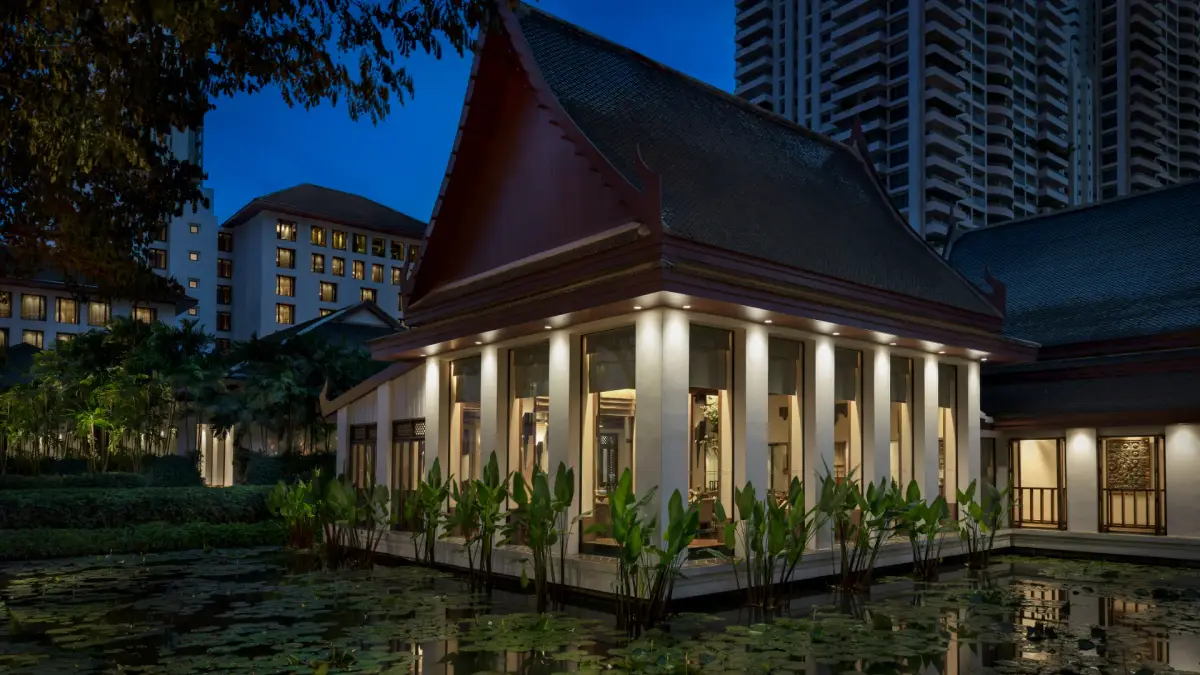 A Thai roofed pavilion lit from inside, standing in a lotus pond at dusk