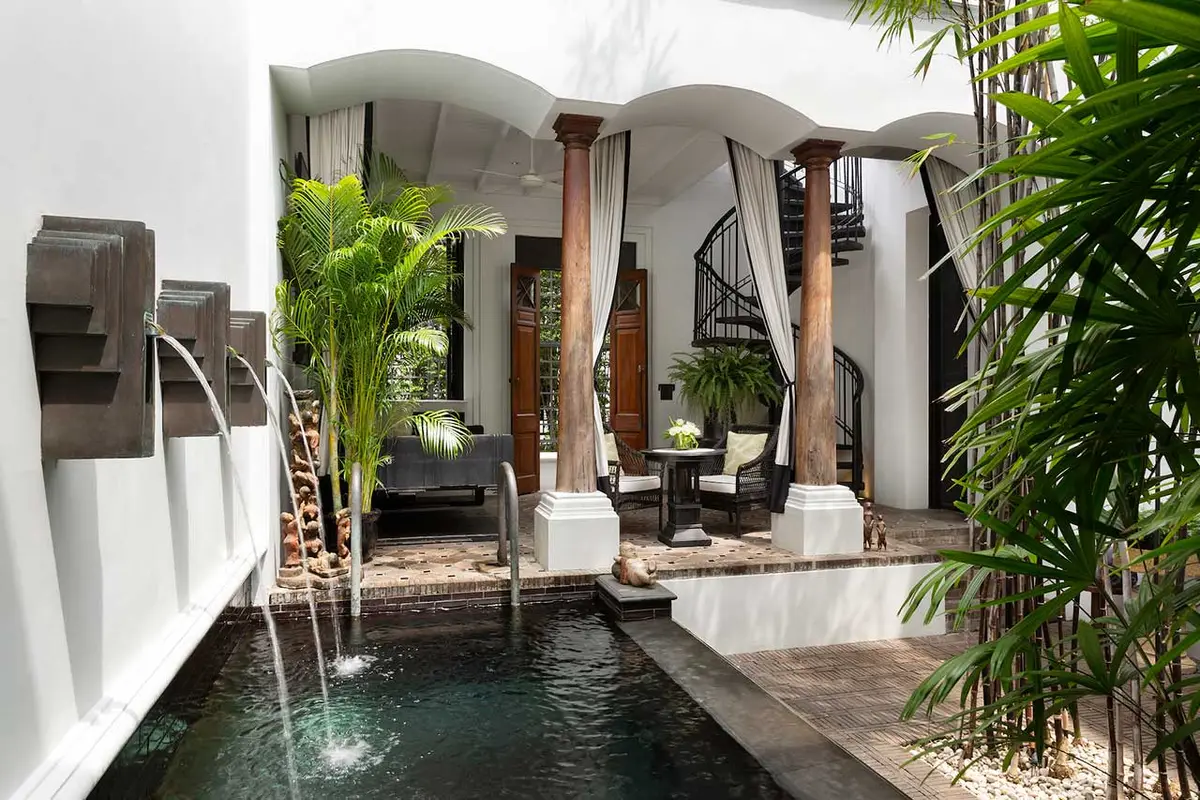 A narrow private plunge pool with water spouts in a planted courtyard between white walls