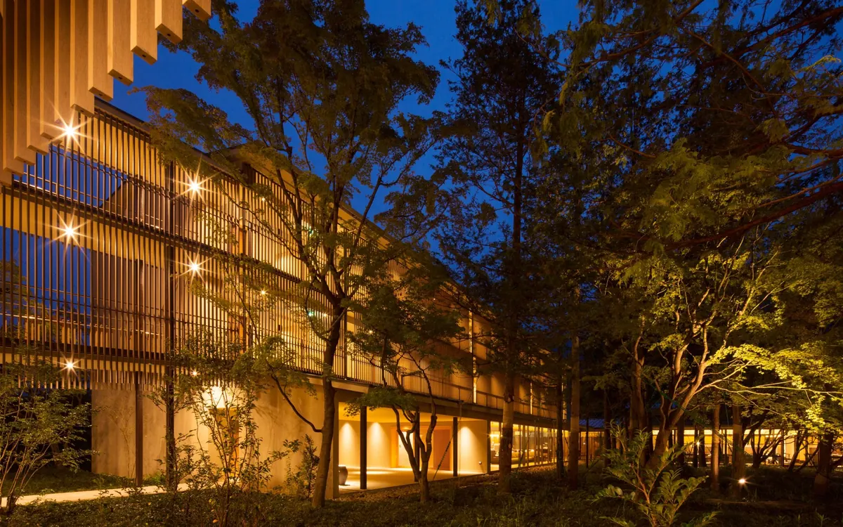 KAI Kinugawa, exterior at dusk with illuminated timber facade and trees, Nikko