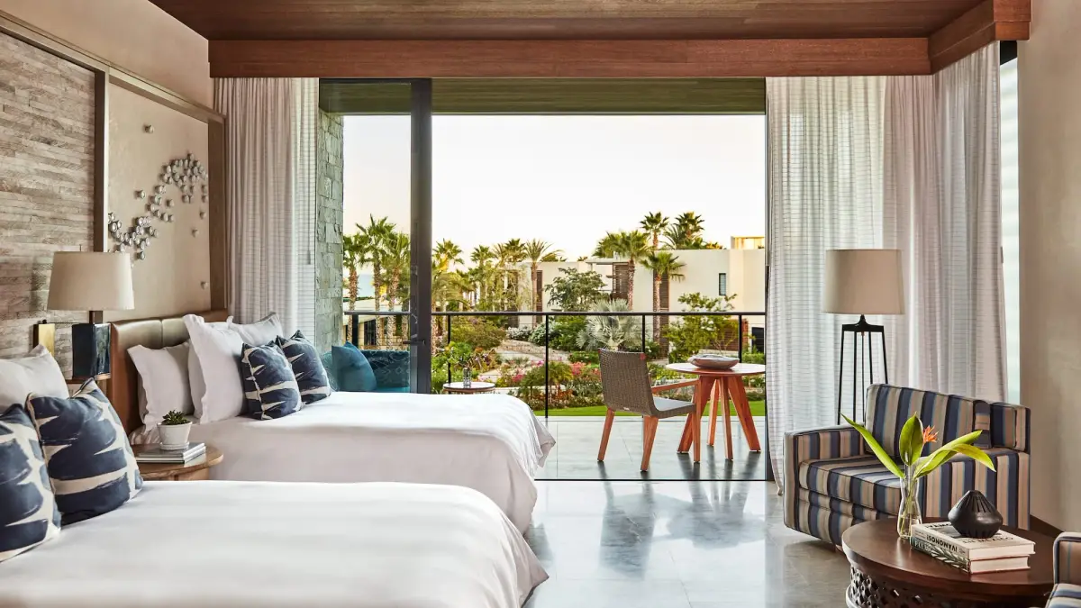 A bedroom with two beds, a striped chair and glass doors onto a terrace over the gardens