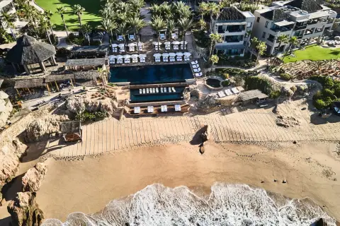 A resort of tiled roofs above a pool and a small cove with a strip of sand
