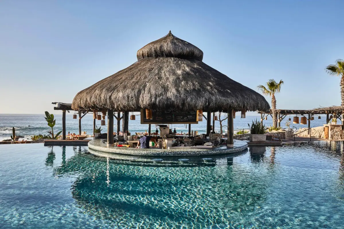A thatched round bar standing in the middle of a turquoise pool above the sea