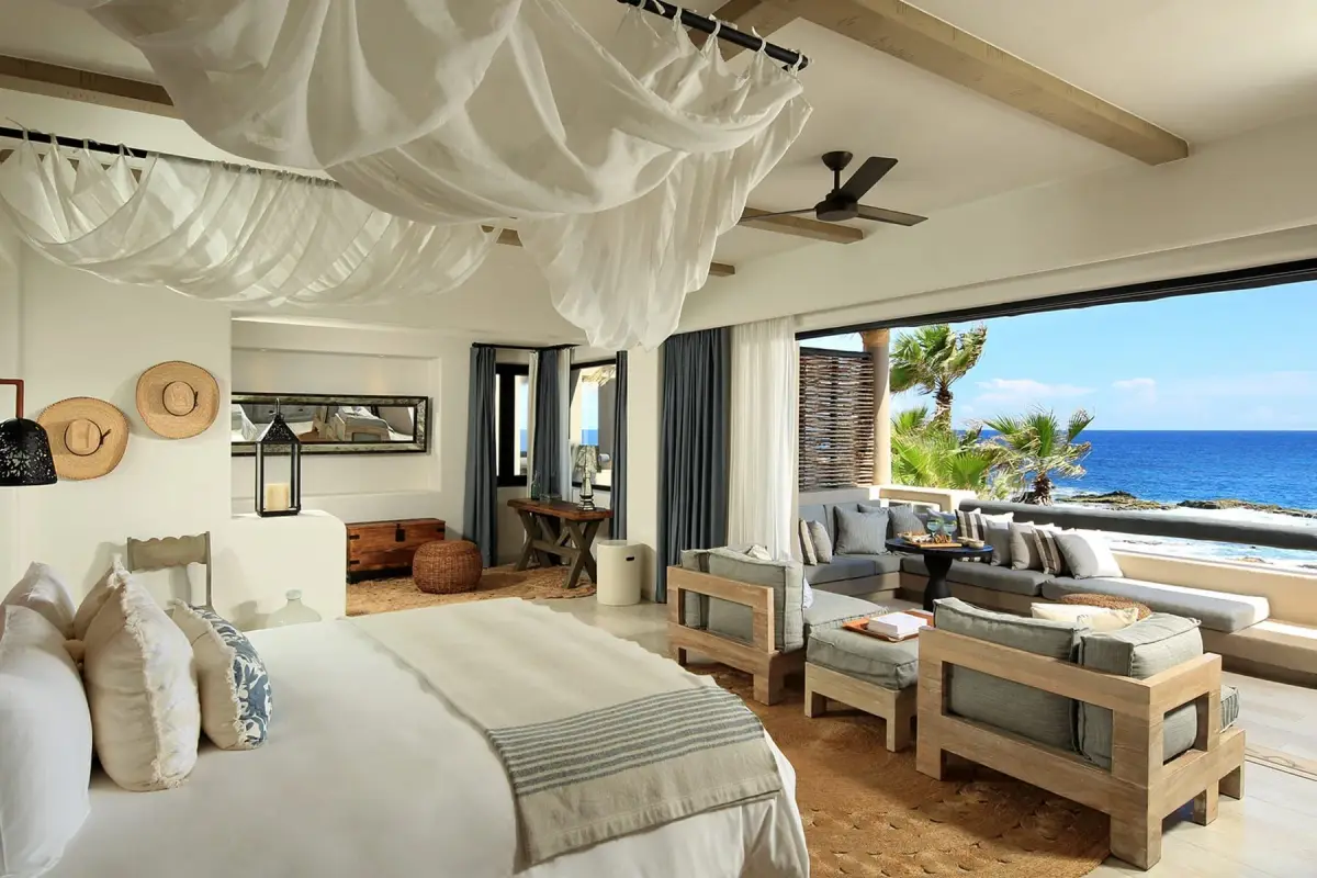 A bed under white drapes in a room that opens along one side to the sea