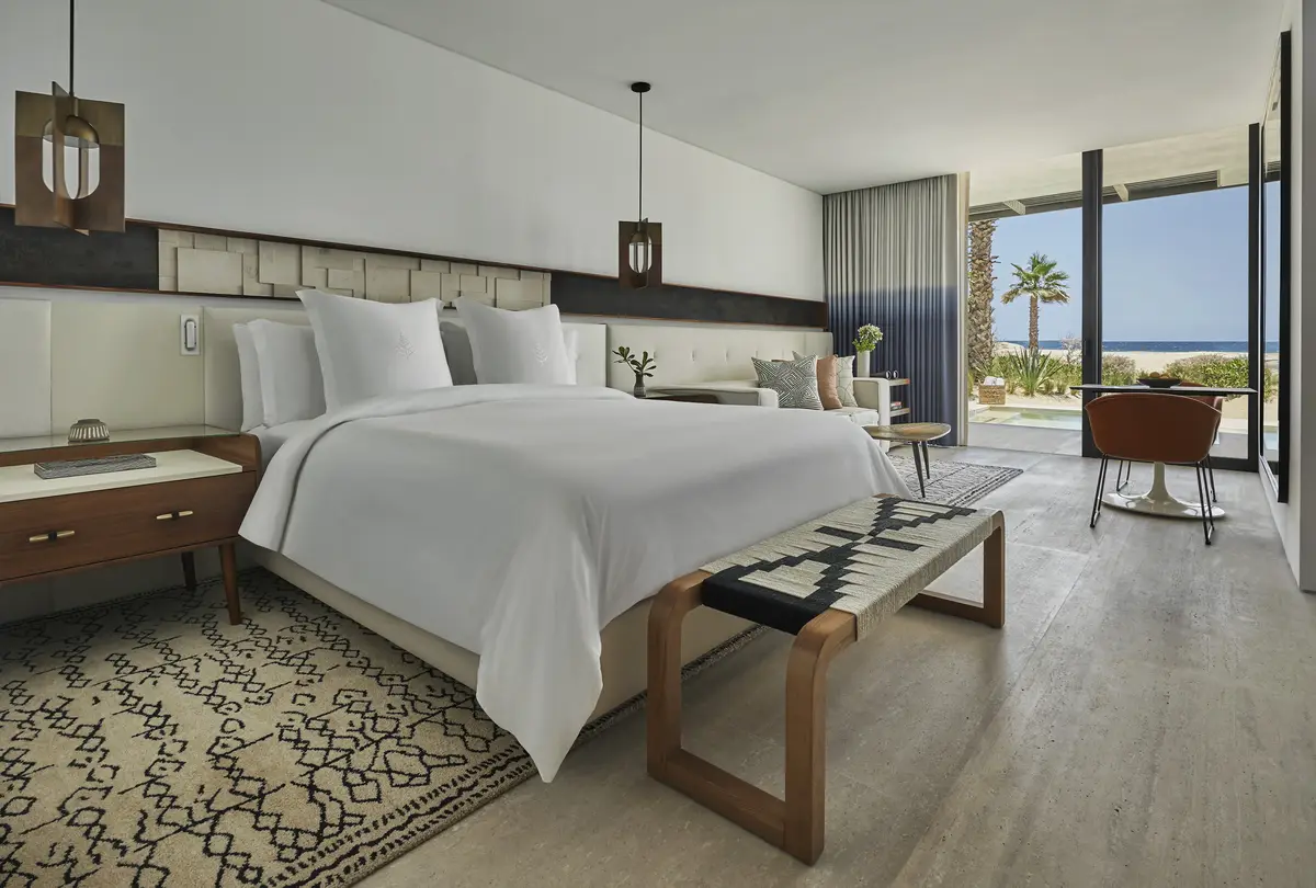 A bedroom with a patterned rug, a bench at the foot of the bed and doors onto a terrace