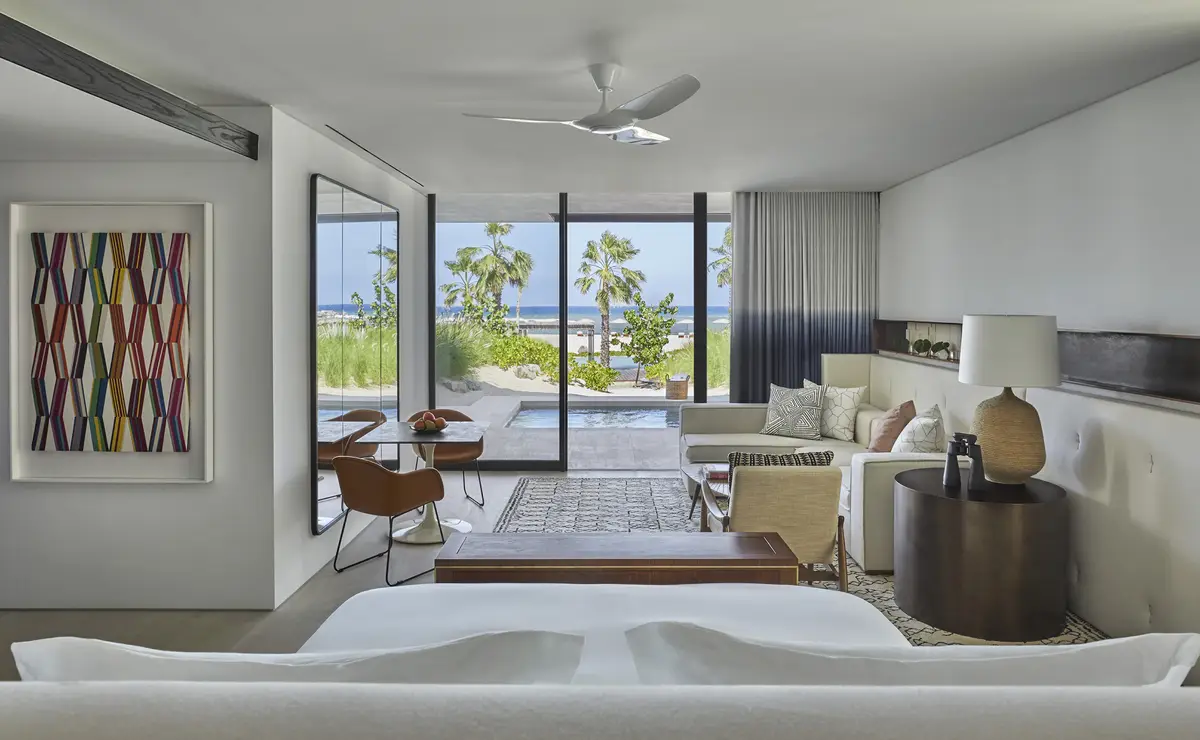 A suite living room in cream and pale wood opening onto a private pool and palms