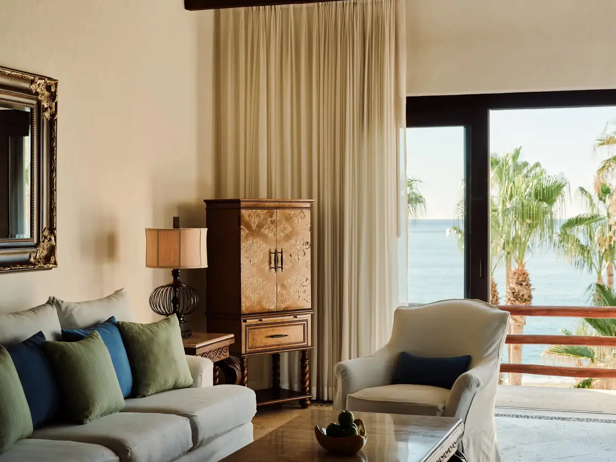 A cream living room with a sofa, armchairs and a doorway onto the sea