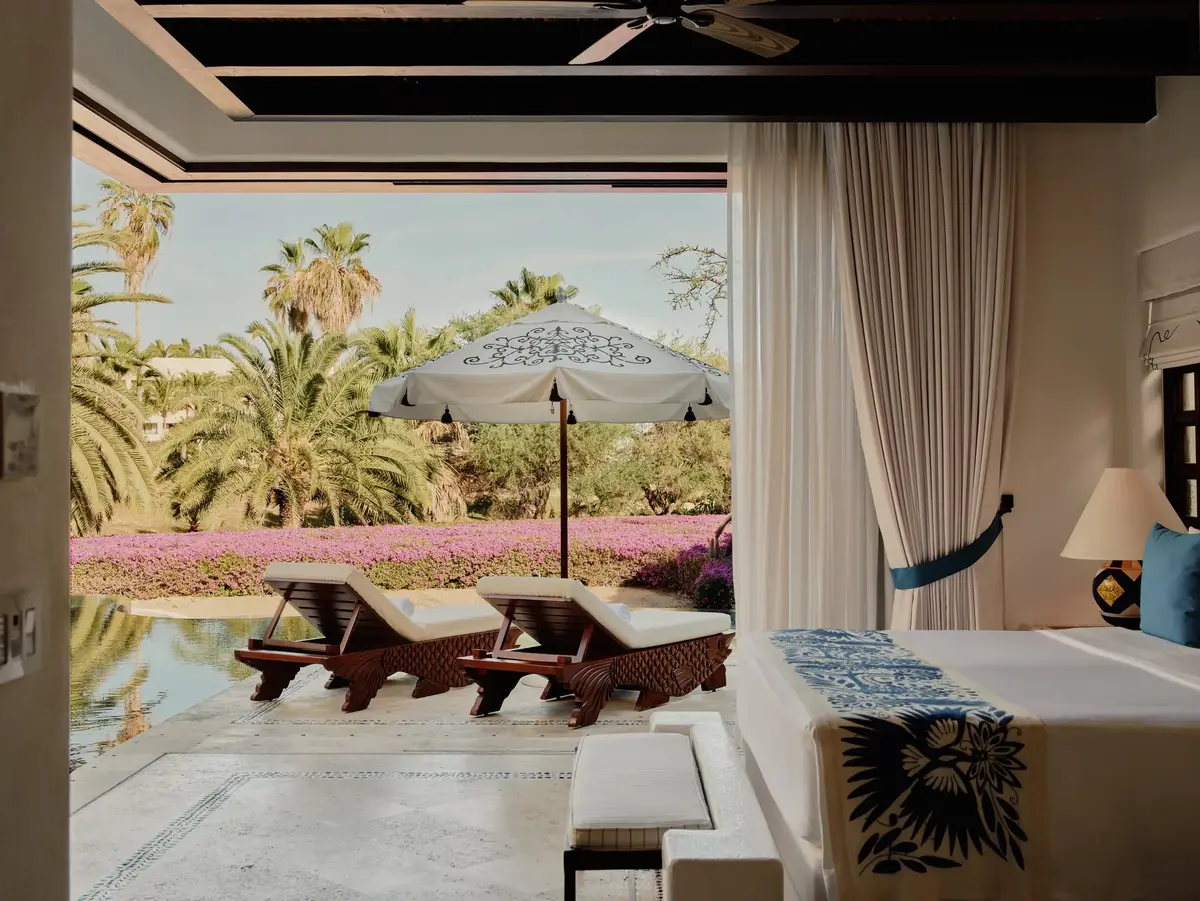 A bedroom opening onto a terrace with loungers, a parasol and flowering shrubs