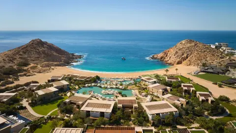 A horseshoe bay of pale sand with a low resort and pools set back behind it