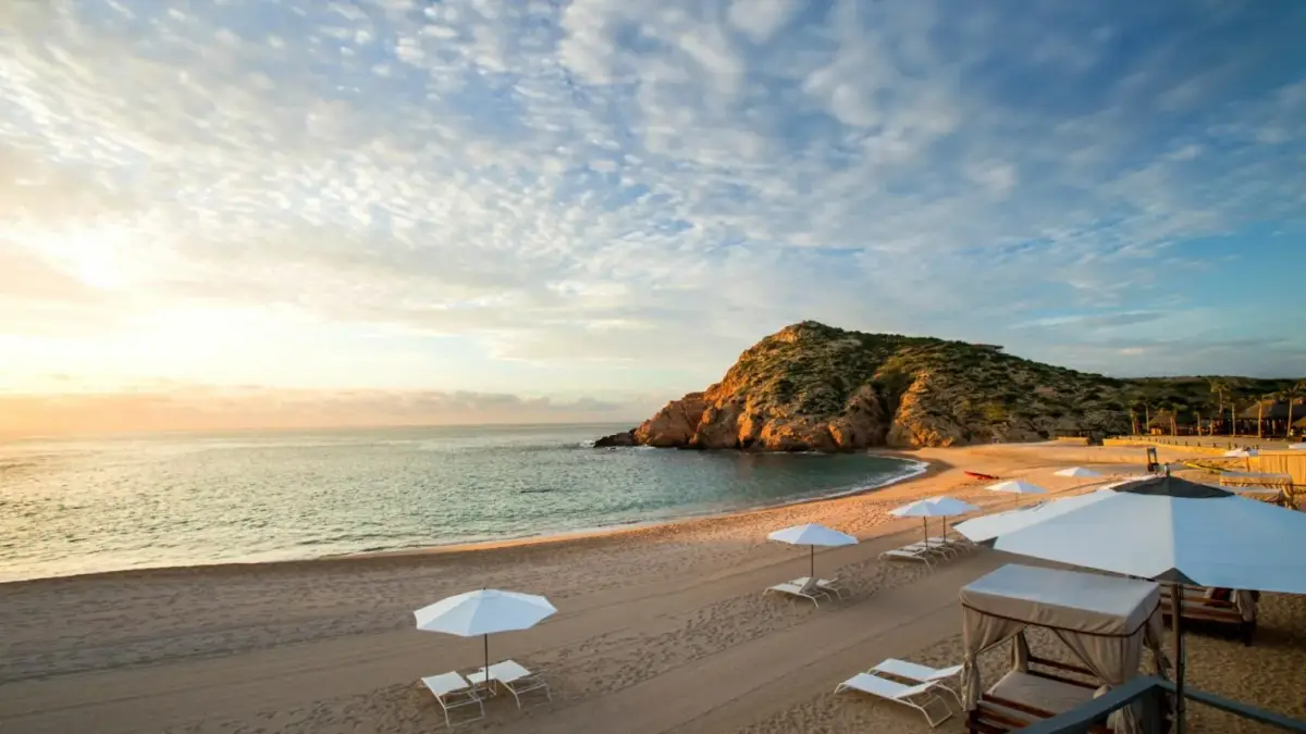 An empty curve of sand with parasols and a rock headland at the far end