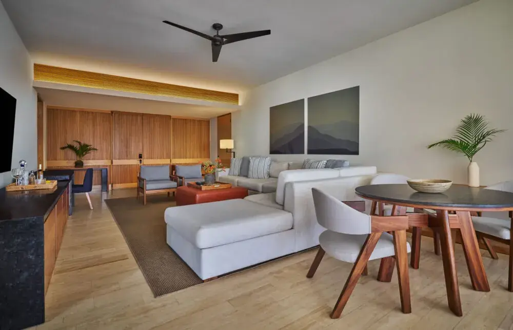 A suite living room with a white sofa, a wooden dining table and a wet bar