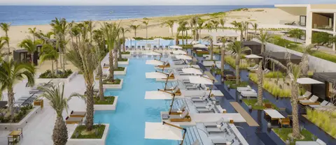 A long narrow pool lined with loungers and planted islands running towards the beach