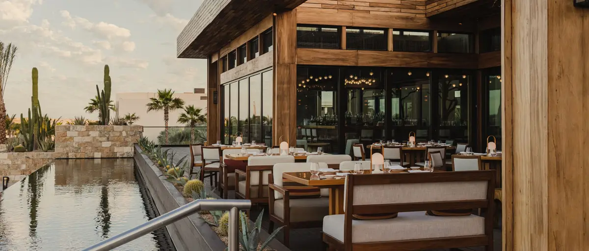 A dark timber restaurant standing over a still channel of water with cacti around it