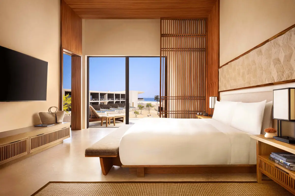 A bedroom with a low platform bed, timber screens and doors onto a terrace above the sea