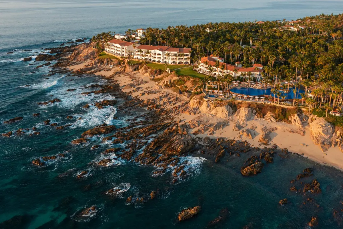 A low white resort spread across a rocky point with palms and two bays either side