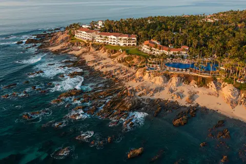 A low white resort spread across a rocky point with palms and two bays either side