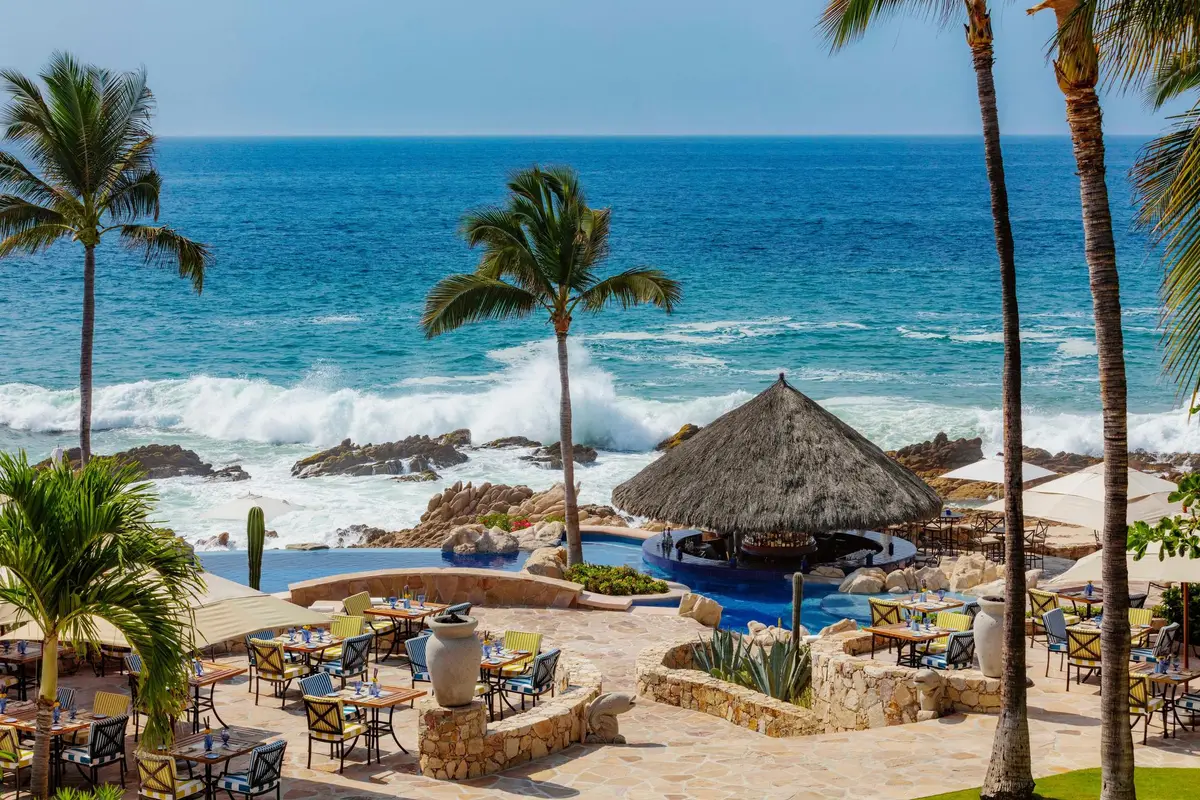 Tables under palapas on a rocky shore with waves breaking behind them