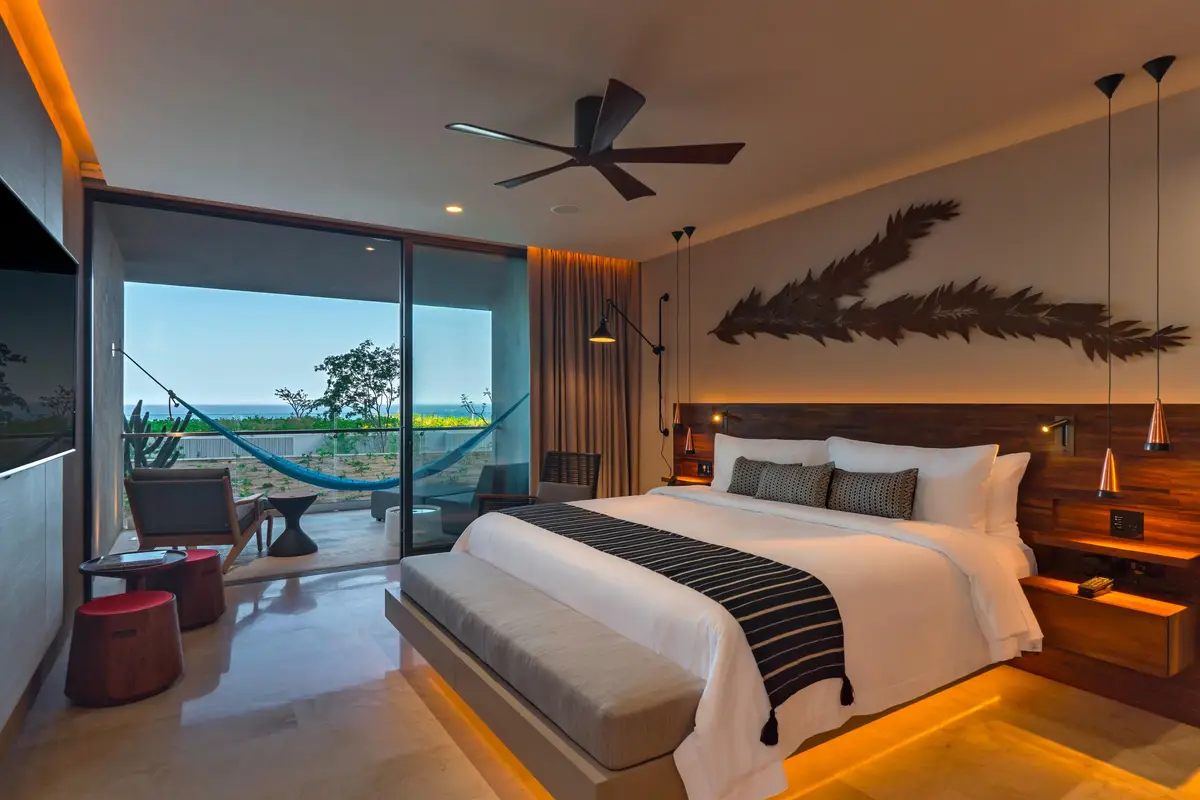 A bedroom with a dark timber headboard, a desk and glass doors to a terrace with a hammock
