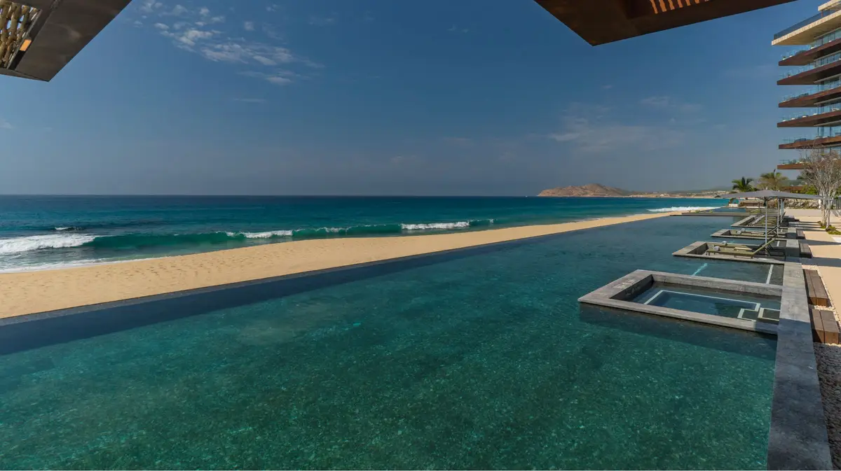 An infinity pool running the length of a beach with a headland in the distance