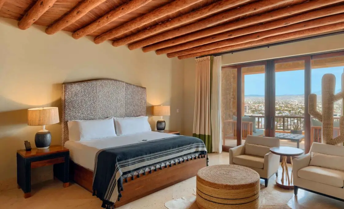 A bedroom under a beamed ceiling with glass doors opening onto a terrace above the bay