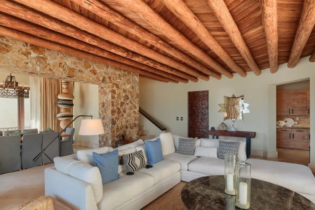 A pale living room with stone walls, a beamed ceiling and deep white sofas