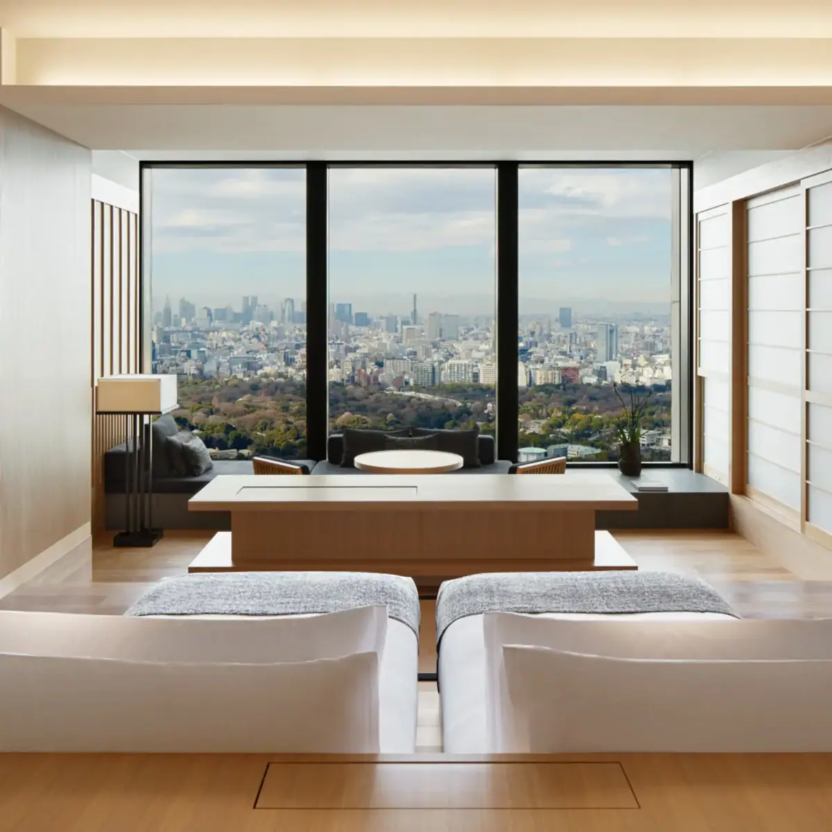 A bedroom with a low bed and floor to ceiling windows over a grey city