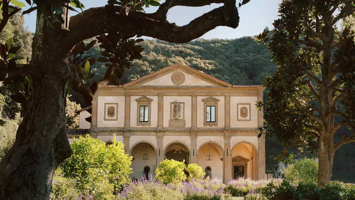 A pale Renaissance facade framed by an old tree on a wooded hillside