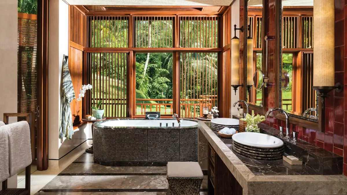 An open bathroom with a stone tub looking out through timber shutters into jungle